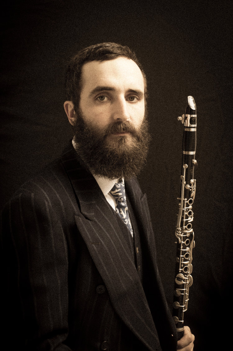 A bearded man sitting with a clarinet.